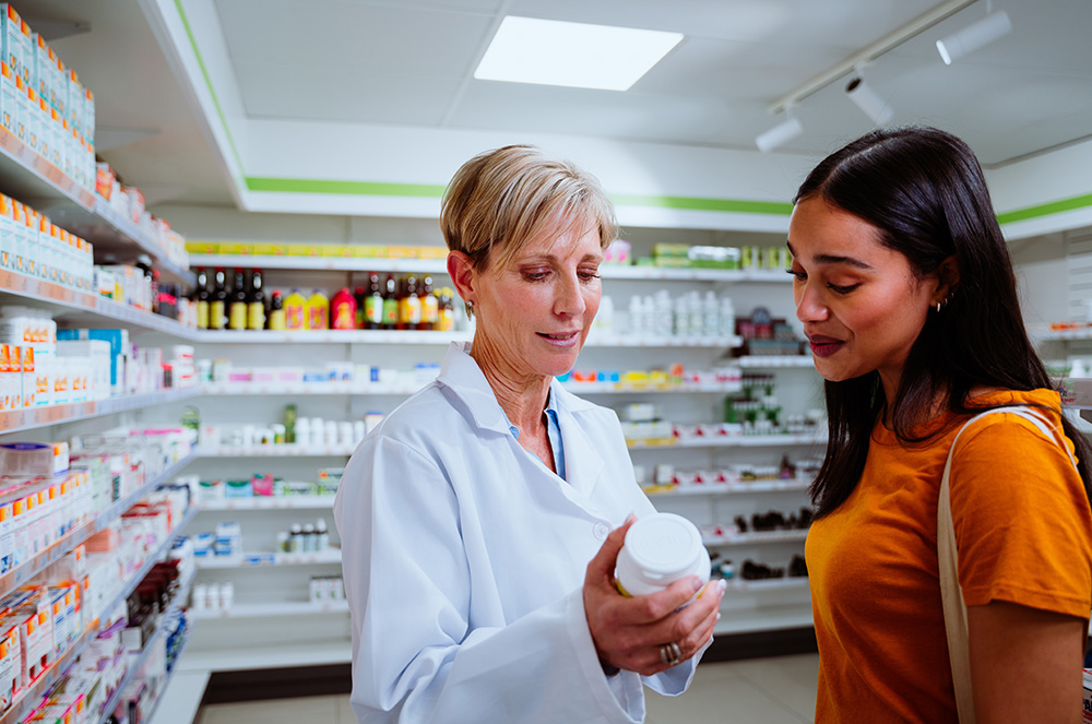 Caucasian senior pharmacist assisting mixed race female patient purchasing medication from the drugstore pharmacy.