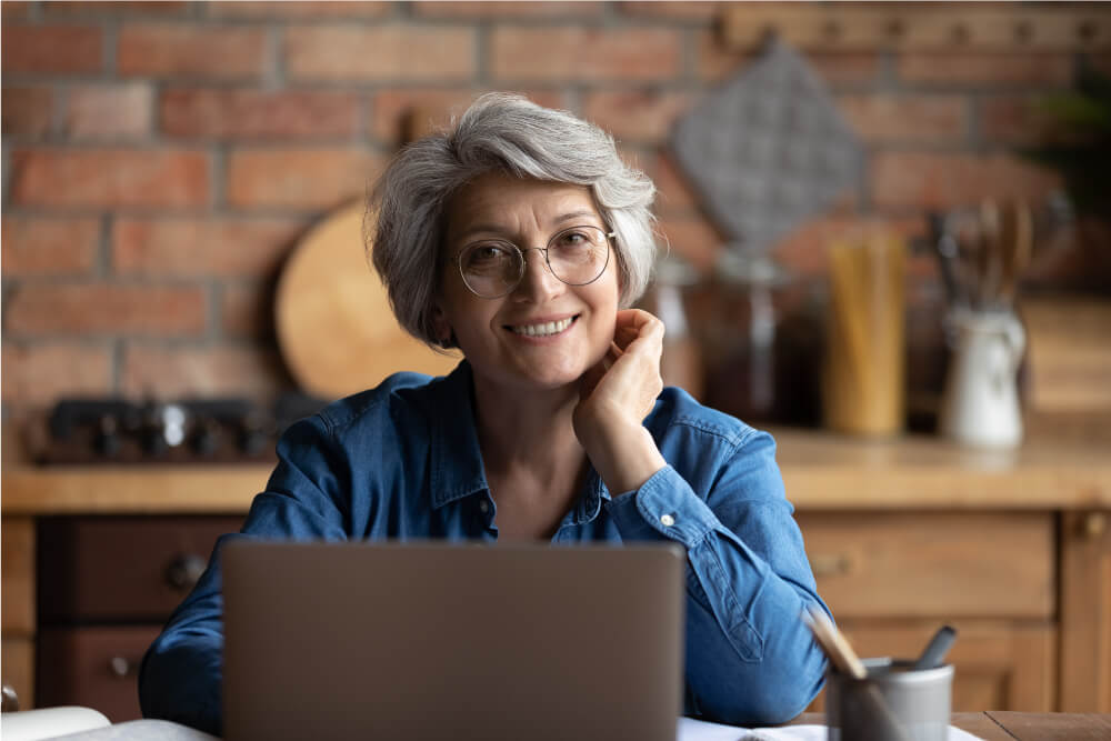 Headshot portrait of happy senior aged hispanic female sit at desk using a laptop